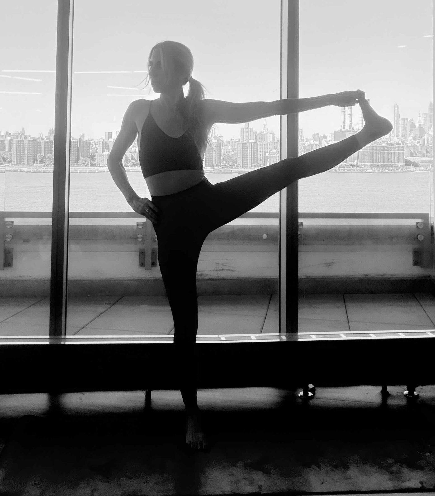 Danya Merson in a standing yoga pose, silhouetted against a window and the city skyline