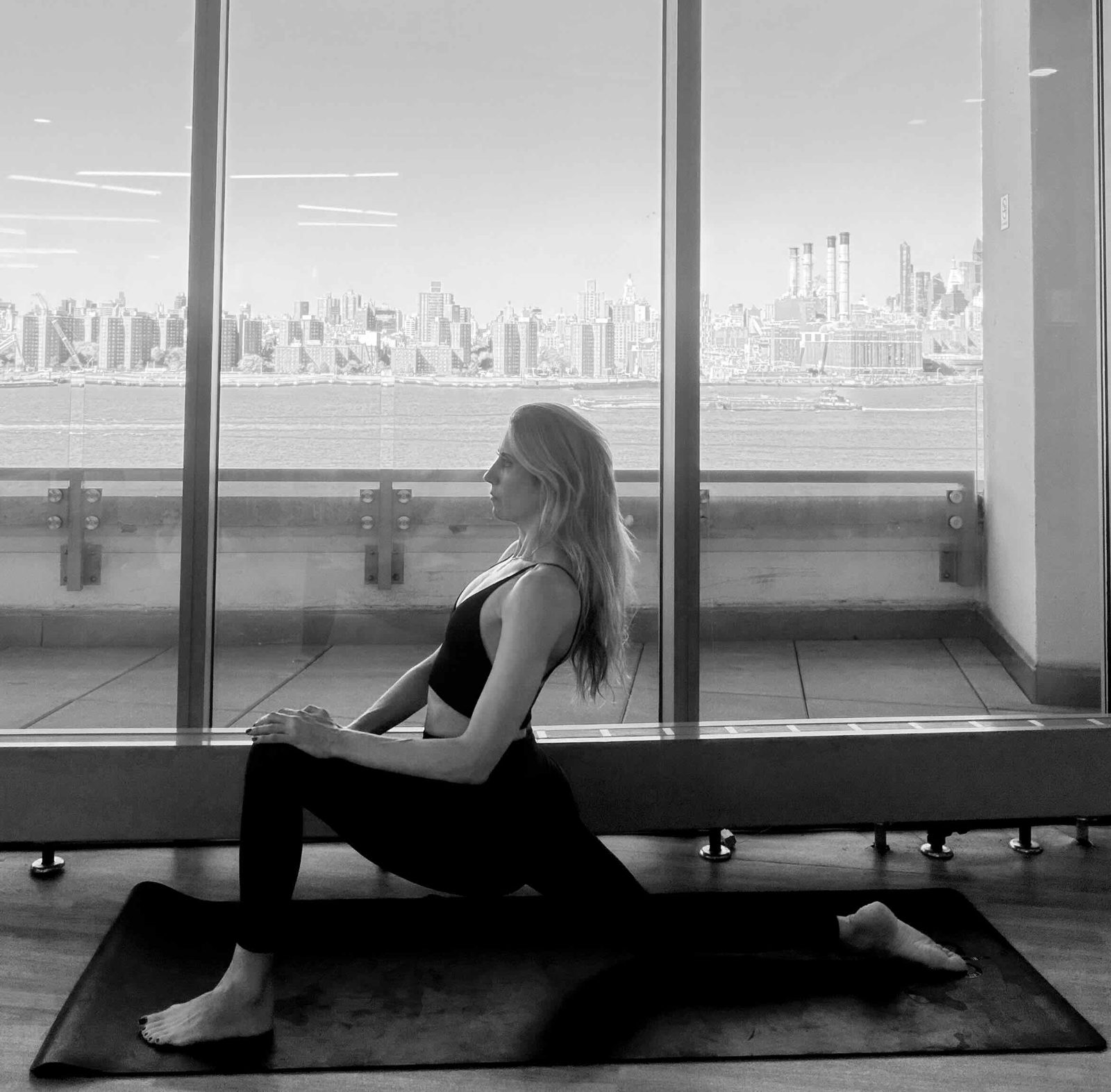 Danya Merson in a low lunge twist beside floor-to-ceiling windows